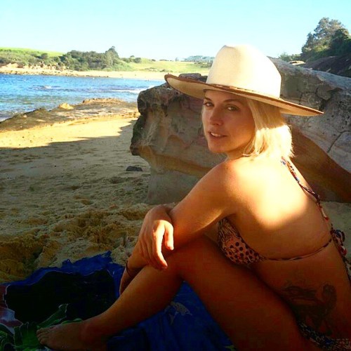 A girl sits on a deserted beach with a sunhat